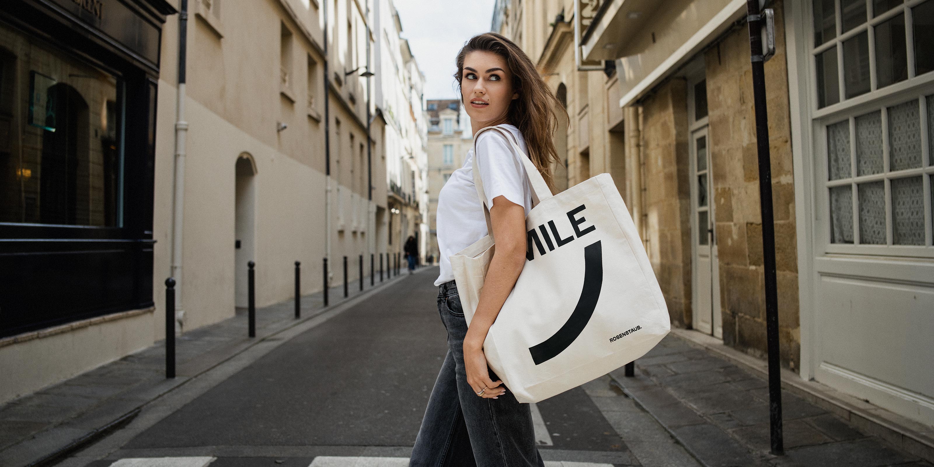 Model crossing a street in Paris carrying the Smile Bag canvas tote by Rosenstaub