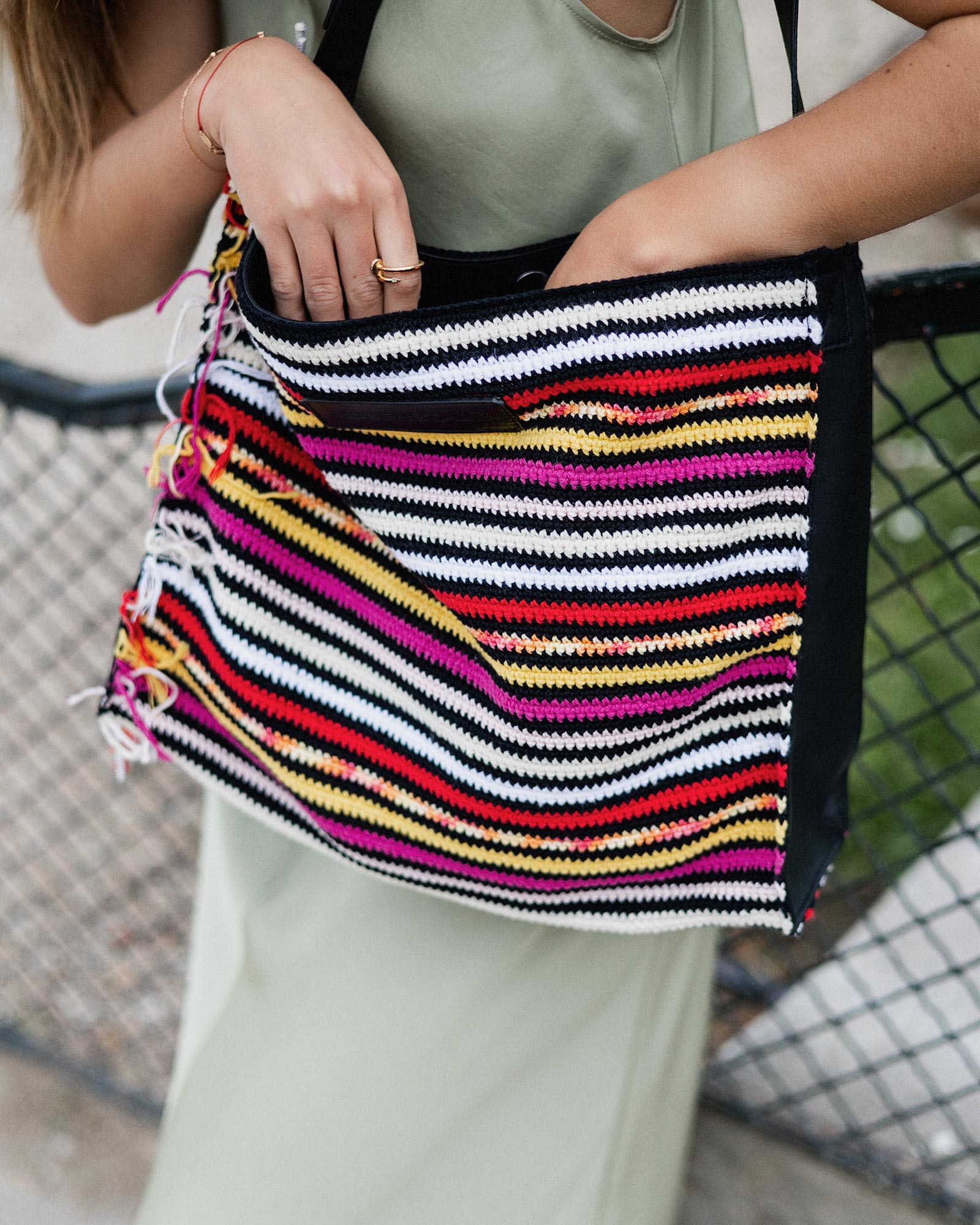 Close-up of the Rosenstaub Crochet Shopper No. 20 of 30 in pink, red, yellow, and white, worn by a model in a park in Paris