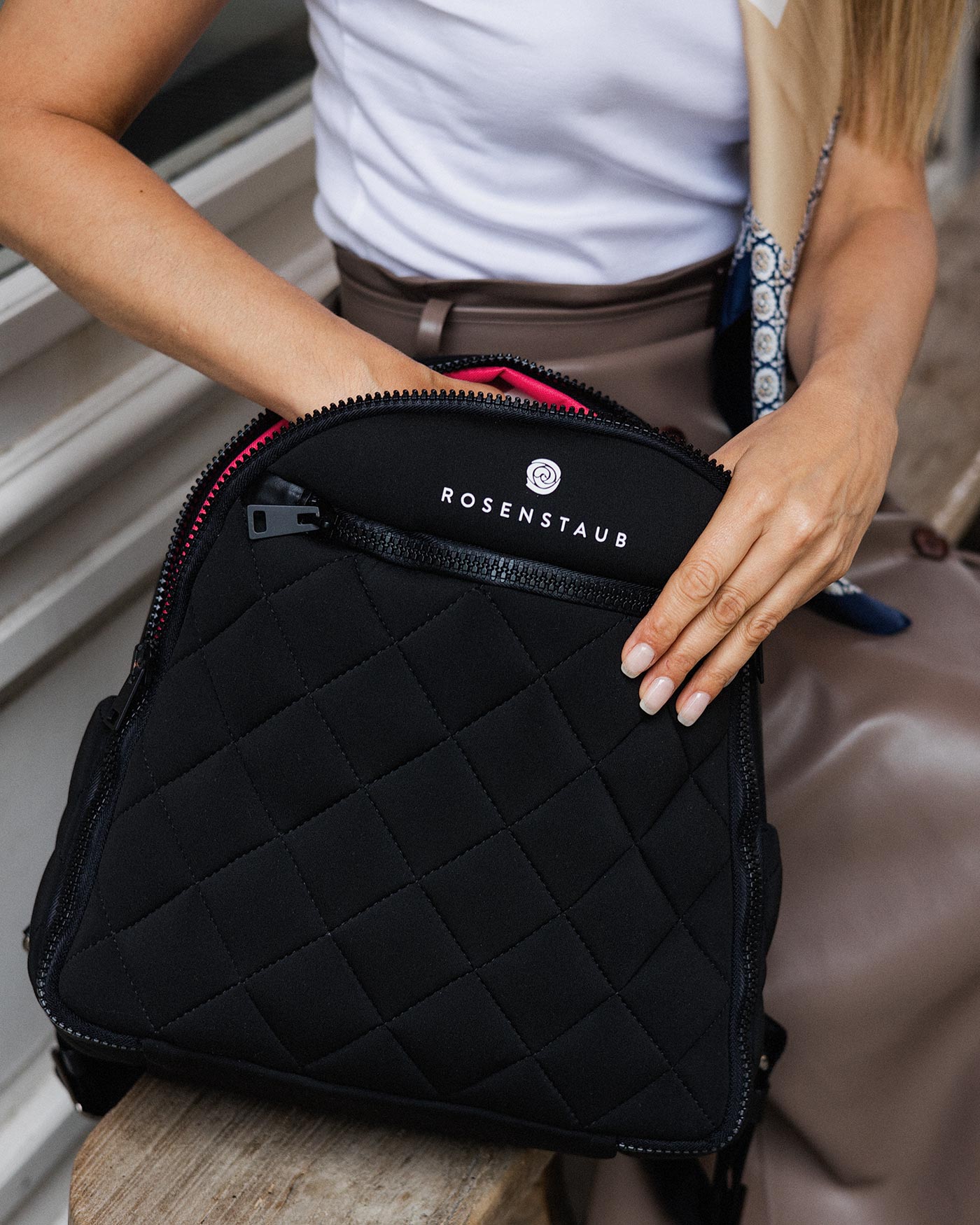 Close-up of a woman placing her hand inside the Rosenstaub Yulex backpack with the pink inner lining subtly visible